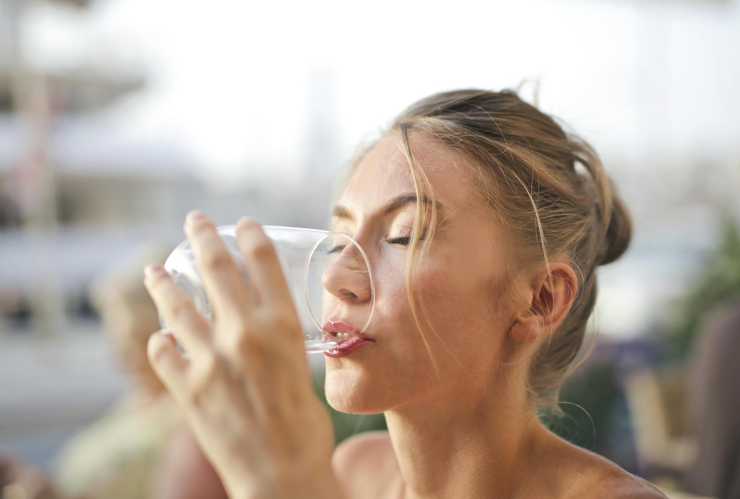 Close-up of a woman drinking water with a serene expression outdoors.